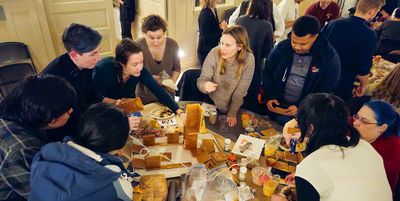 Lund Opsahl employees gather around a large table with gingerbread house making supplies in the middle.